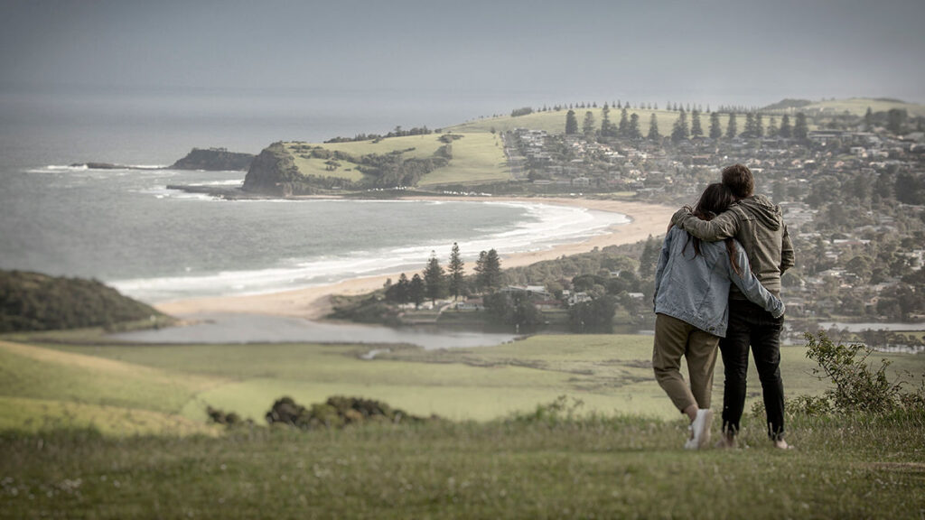 Two people standing together looking out over a south coast headland and township