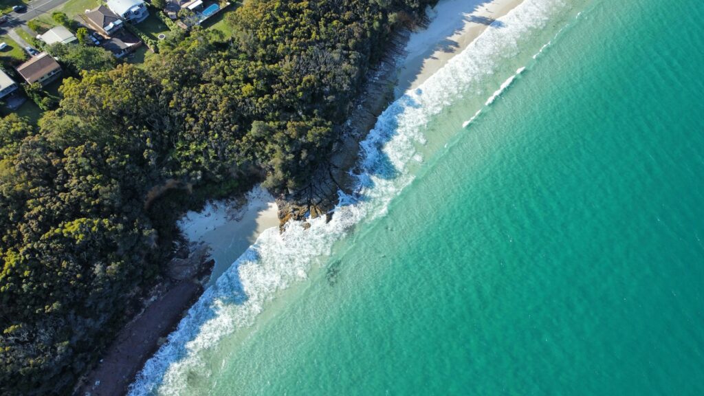 Aerial view of white sand and turquoise water at Jervis Bay with a few houses set back in the bush