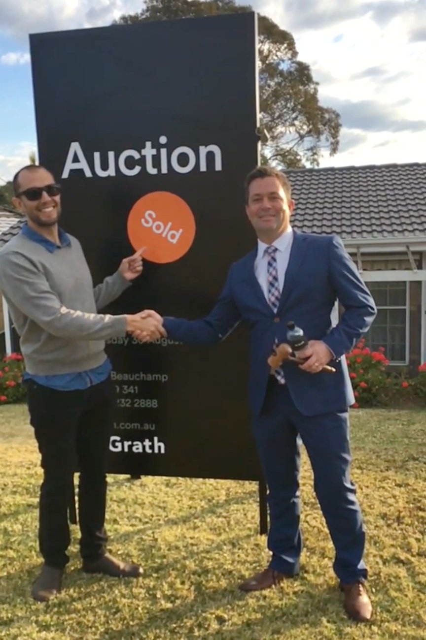 Matt Knight of Precium shaking hands with a client in front of a SOLD auction board after winning the property at auction