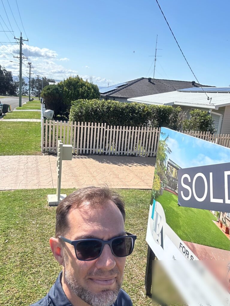 Matt Knight of Precium standing beside a sold board outside a coastal home