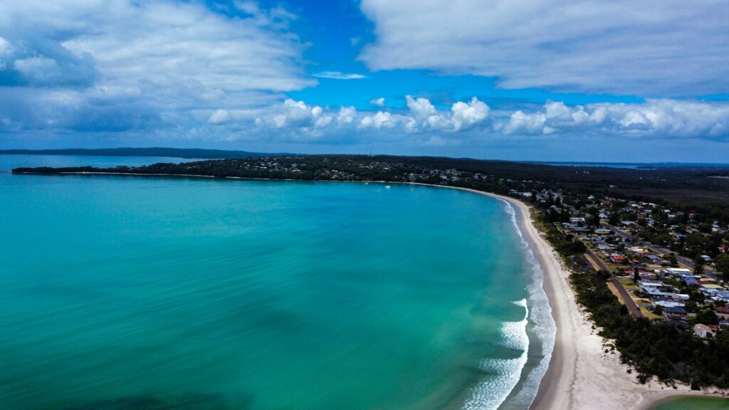 Aerial view of a Jervis Bay beach with houses set along the shoreline and a headland in the distance